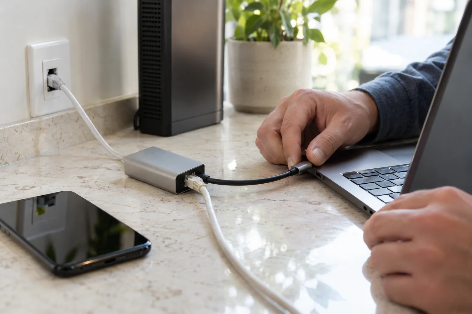 手部在石材工作区连接笔记本与USB-C网络扩展坞,旁边可见手机和家庭网关
